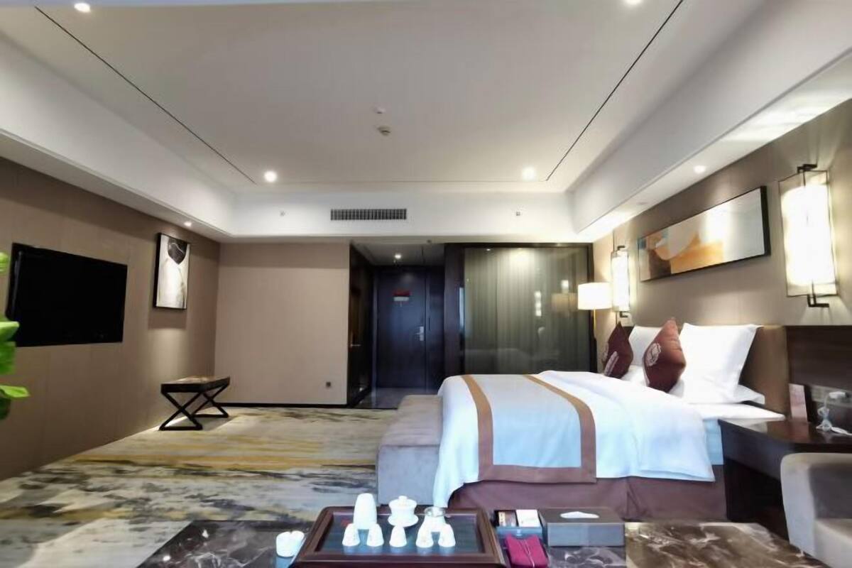 A hotel room with a bed, bedside table, lamp, and a chessboard on the floor.