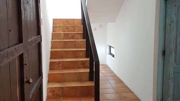 Una escalera de madera con barandillas negras que lleva a un rellano con un pequeño ventanal.