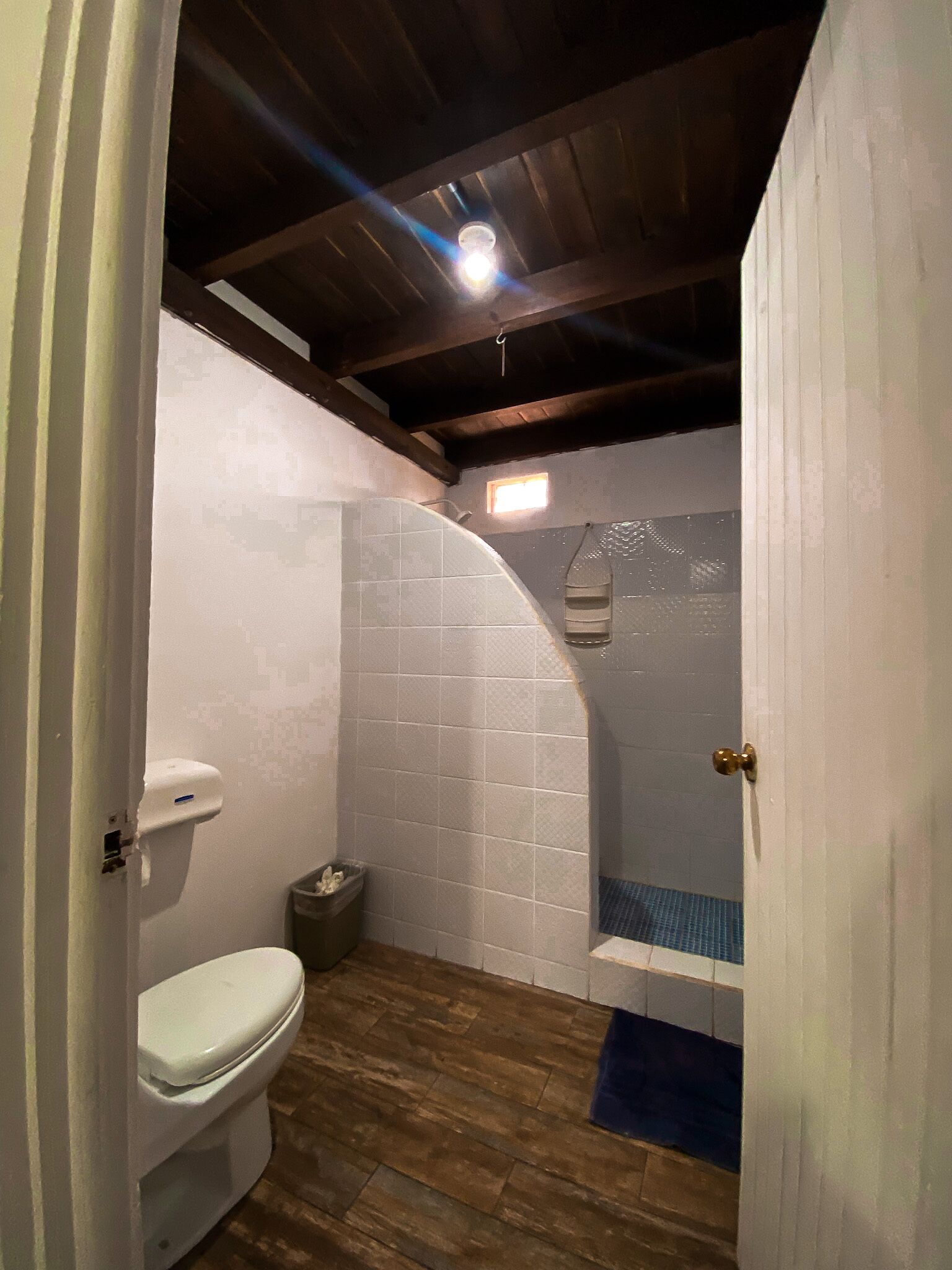 Un baño pequeño y funcional con inodoro, zona de ducha y piso de madera.