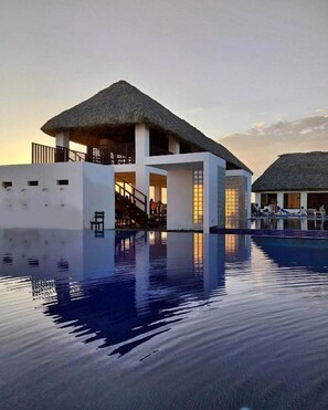 A resort with a swimming pool, a thatched-roof building, and a white structure with a balcony.