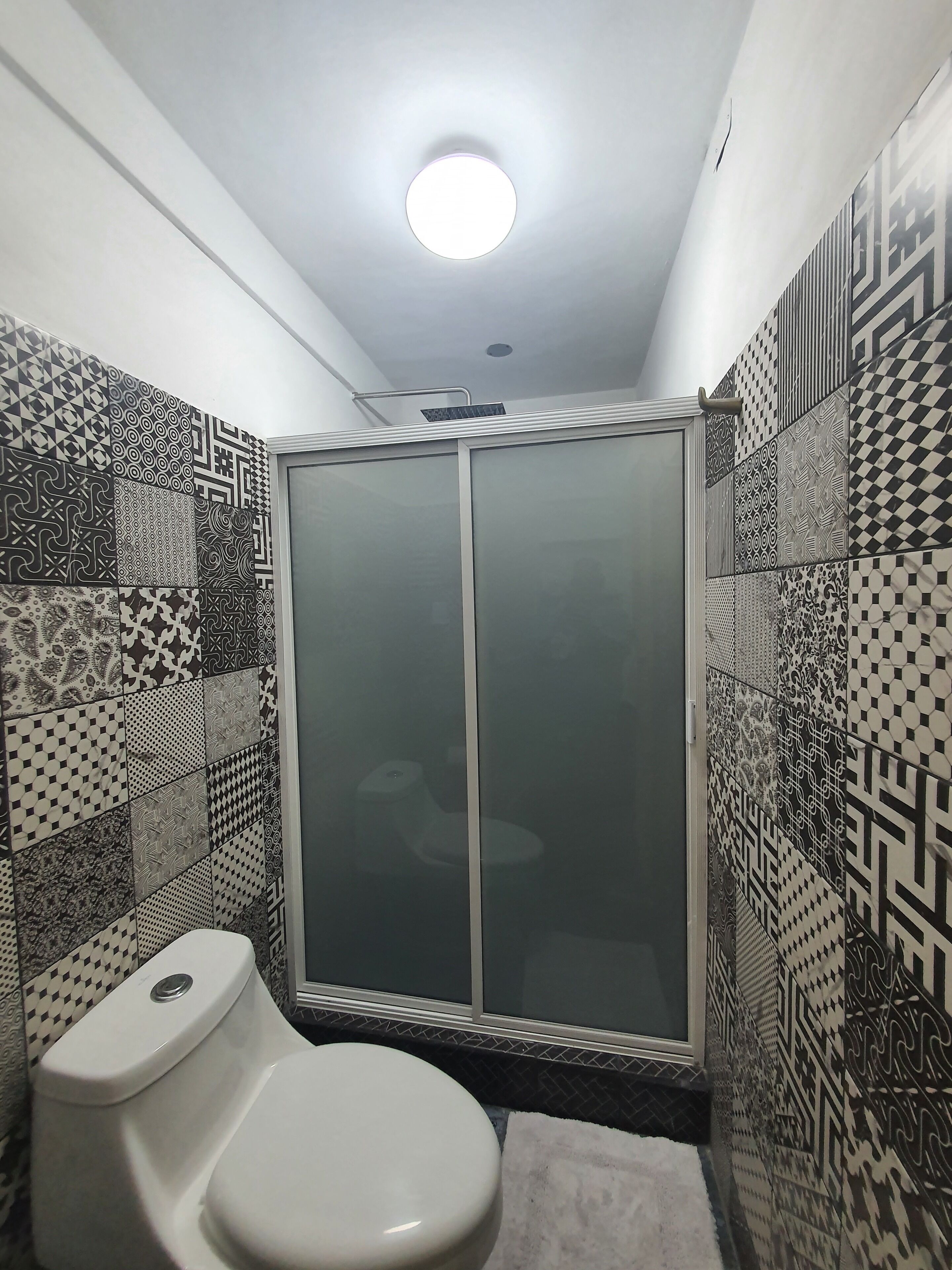 Een badkamer met toilet, een douche met glazen deur en behangtegels op de muren.