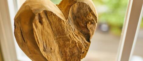 A wooden heart-shaped object with a rough texture, possibly a sculpture, displayed indoors with a blurred green background.
