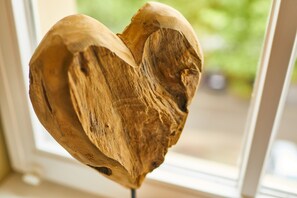 A wooden heart-shaped object with a rough texture, possibly a sculpture, displayed indoors with a blurred green background.