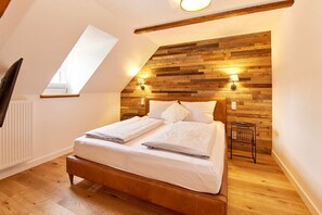 A bedroom with a sloped ceiling, wooden wall paneling, a bed with white linens, and two wall-mounted lamps. - Rochter Landhotel (Zeltingen-Rachtig)