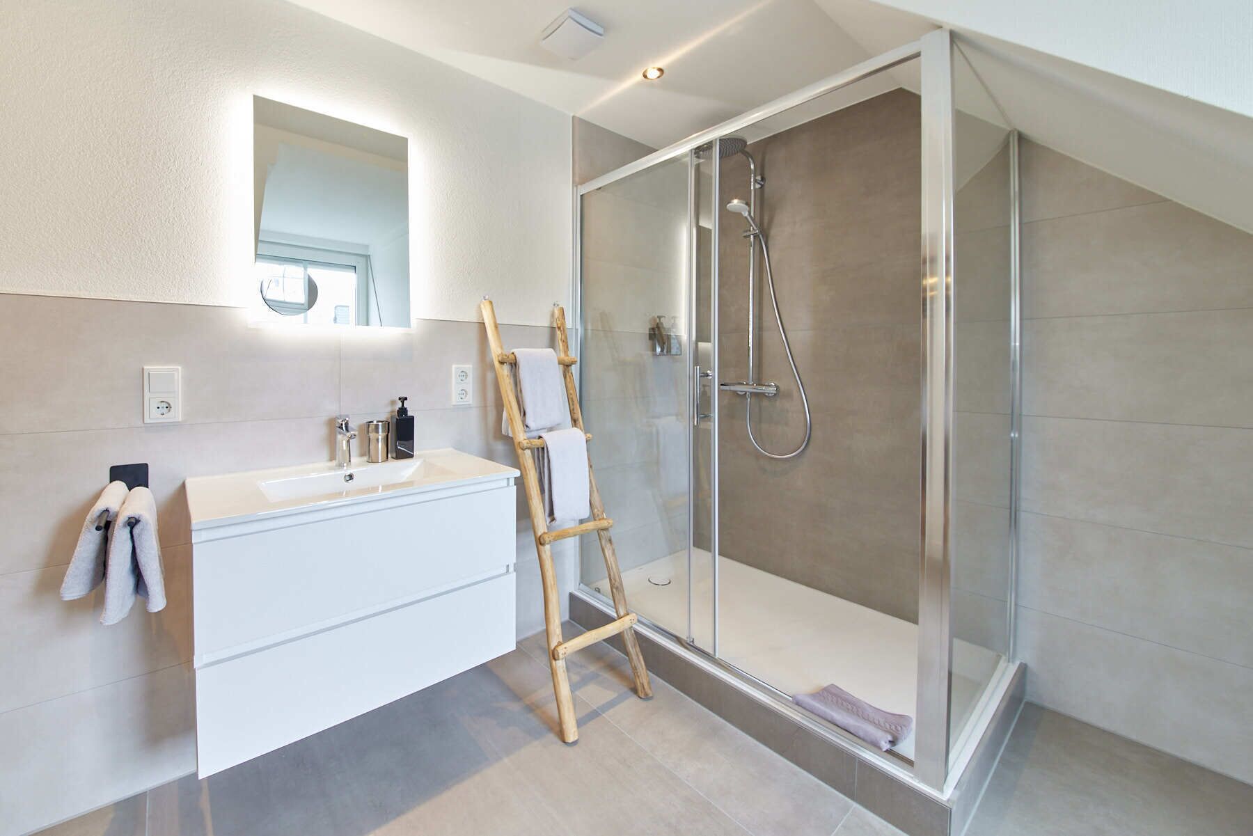 Ein modernes Badezimmer mit einer gläsernen Dusche, einem weißen Waschtisch mit Spiegel und einer Holzleiter.