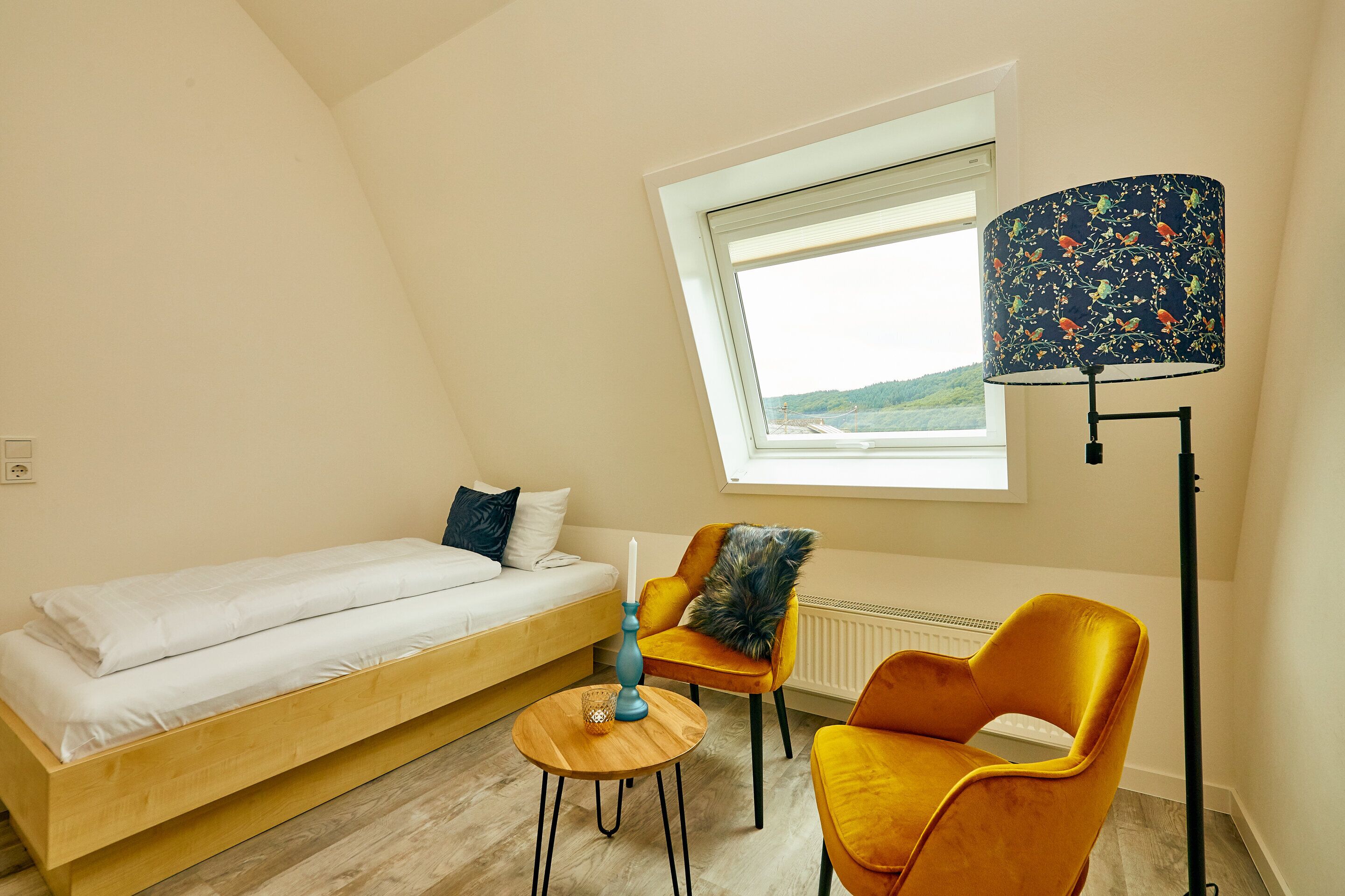 Une chambre avec un lit, une petite table, deux chaises, une lampe et une fenêtre donnant sur un beau paysage.