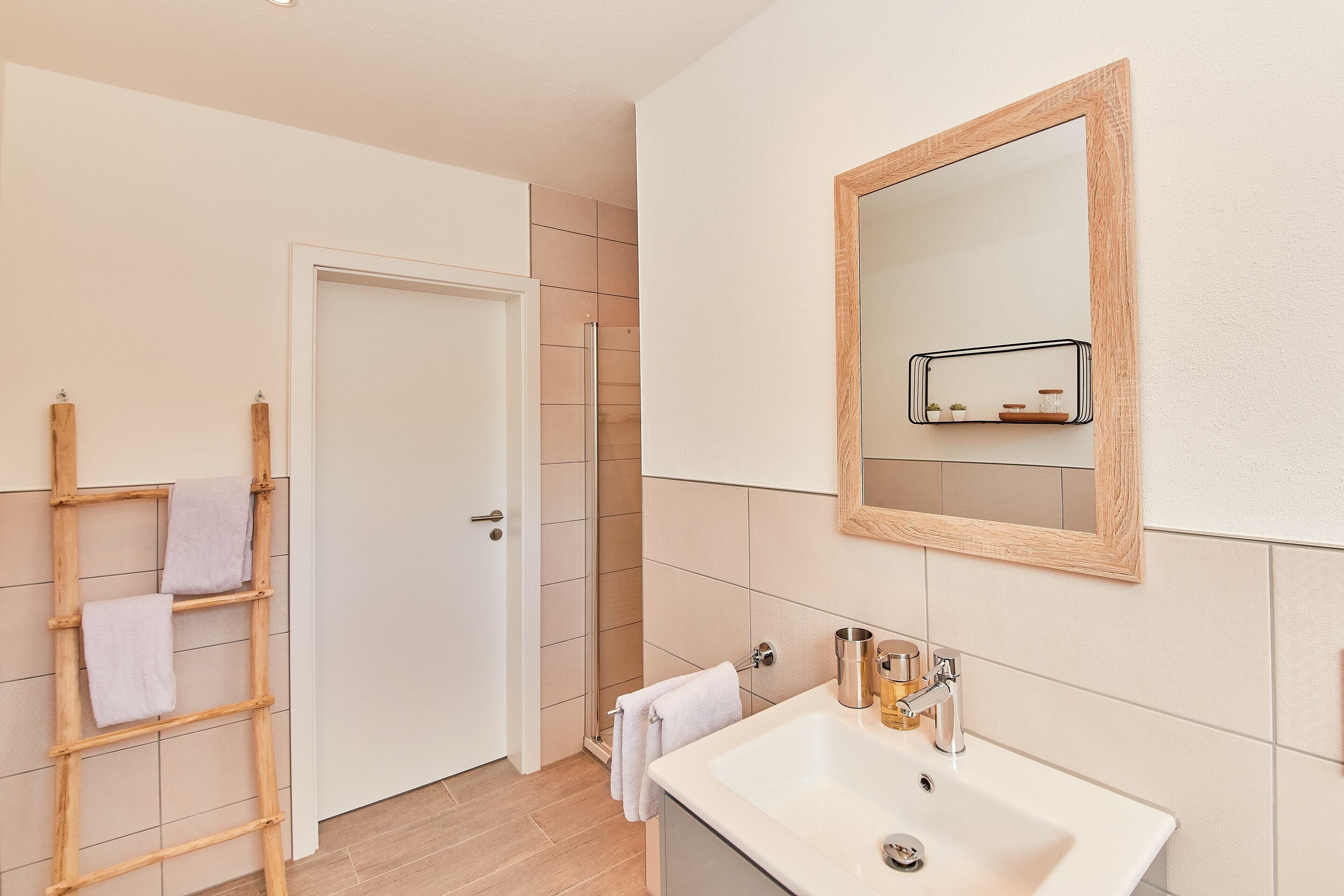 Un bany amb un lavabo blanc, una escala de fusta i una porta que dona a una zona de dutxa.
