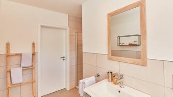Un bany amb un lavabo blanc, una escala de fusta i una porta que dona a una zona de dutxa.