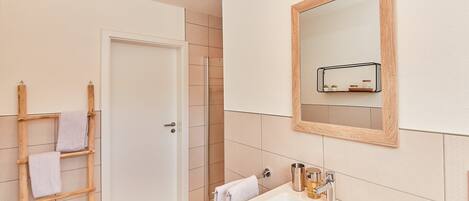 A bathroom with a white sink, a wooden ladder, and a door leading to a shower area.