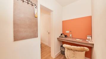 A hallway with a wooden floor, a reception desk with a mirror, a trash bin, and a door leading to another room.