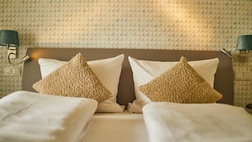 Ein ordentlich gemachtes Bett mit zwei Zierkissen und einem Kopfteil vor einer Wand mit Muster.