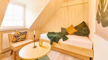 Een gezellige kamer met een schuine kap, een bed met kussens, een klein tafeltje en een raam.