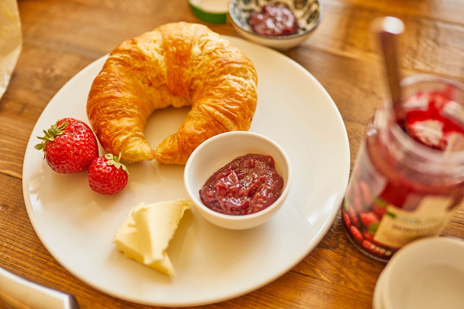 Un piatto con un croissant, fragole e una piccola ciotola di marmellata.