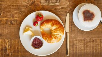 Ein Frühstücksbuffet mit einem Croissant, Erdbeeren und Marmelade auf einem Teller, dazu eine Tasse Kaffee auf einem Holztisch.