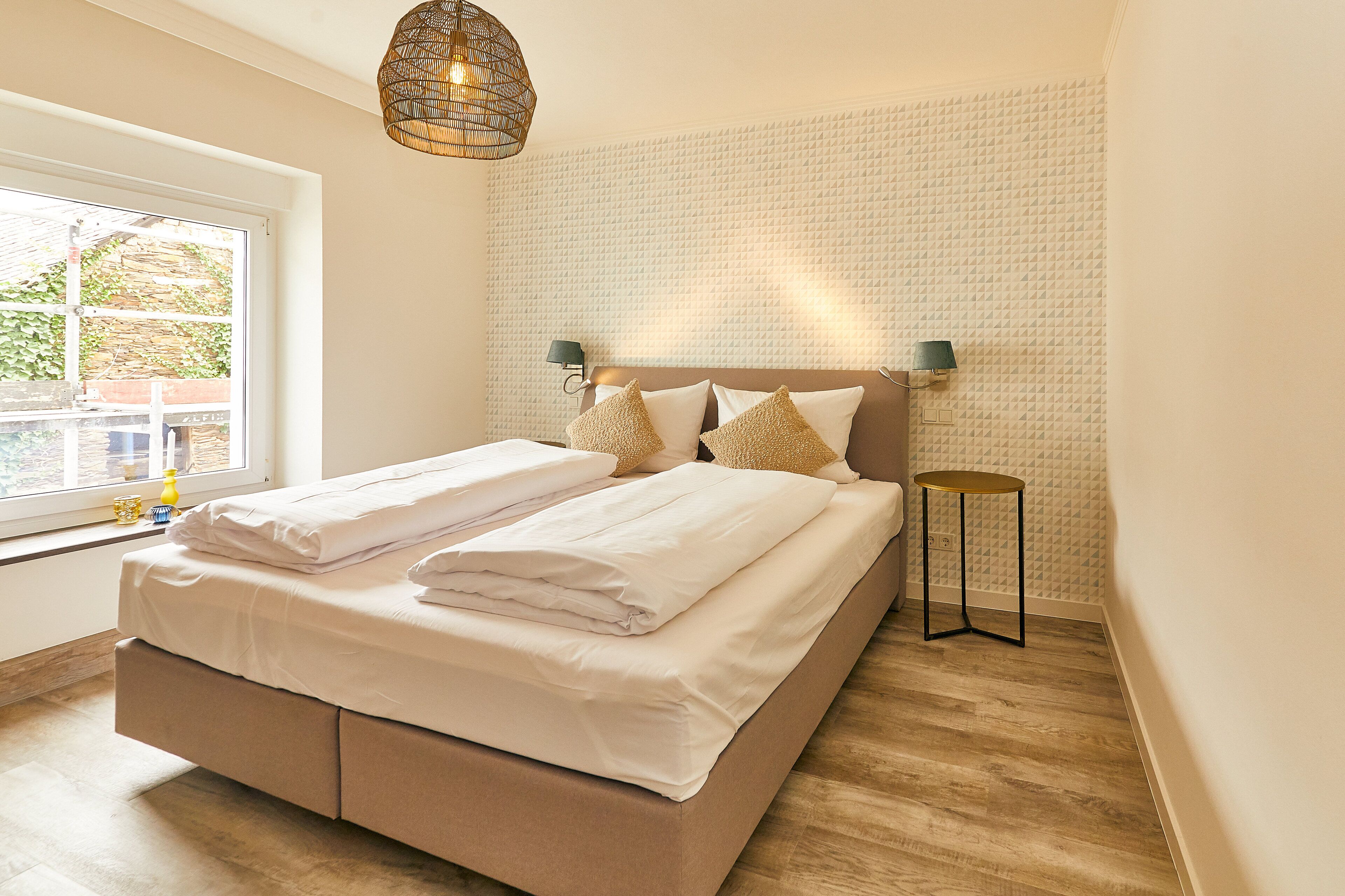 A neatly made bed with white linens, a bedside lamp, and a small round table beside it.