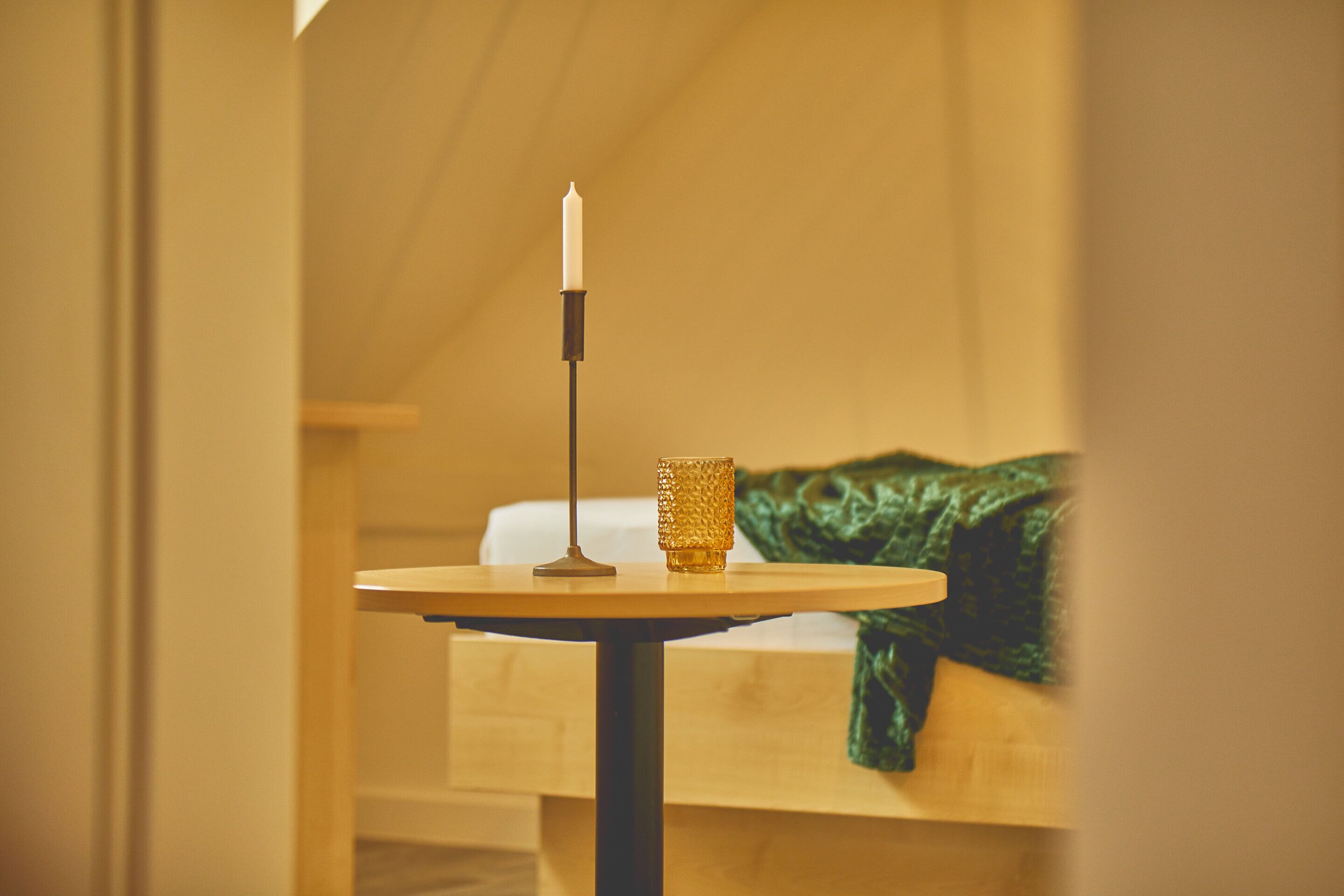 A room with a bed, a table with a candle, and a green blanket.