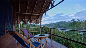 A wooden deck with two lounge chairs and a small table, overlooking a lush landscape and a body of water.