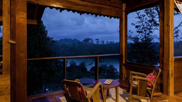 A wooden deck with a view of a forest and water at dusk.