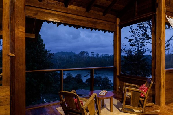 A wooden deck with a view of a forest and water at dusk.