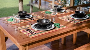 A wooden dining table set with black bowls, plates, and glasses, with colorful placemats.
