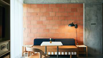 Una habitación con pared de ladrillo, un banco de madera, una pequeña mesa y una lámpara.