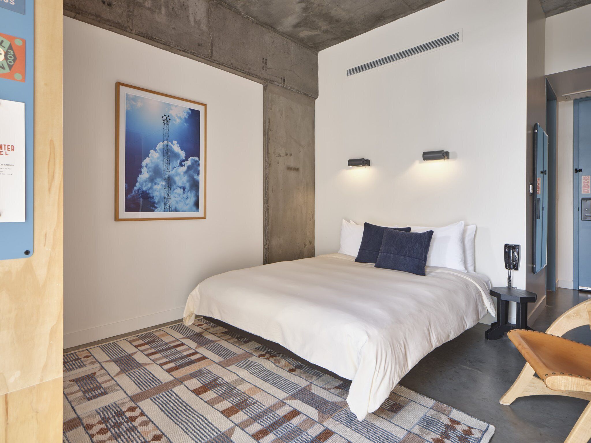 Un dormitorio moderno con una cama grande, un tapete estampado, un cuadro enmarcado en la pared y una silla de madera.