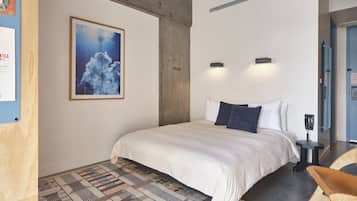Un dormitorio moderno con una cama grande, un tapete estampado, un cuadro enmarcado en la pared y una silla de madera.