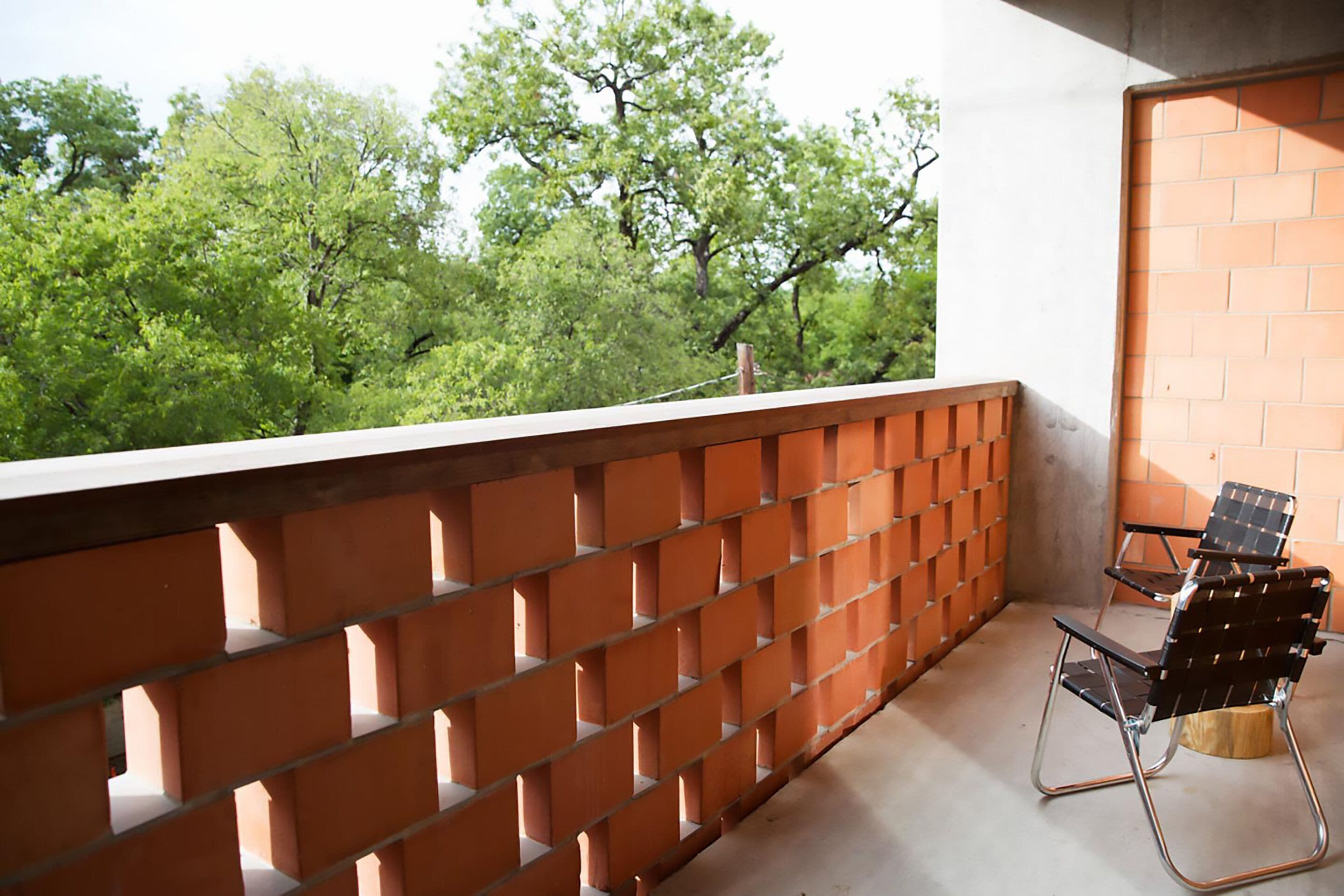 A balcony with a brick wall, two chairs, and a view of green trees.