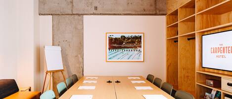 A conference room with a long table, chairs, a whiteboard, and a projector screen displaying "The Carpenter Hotel".