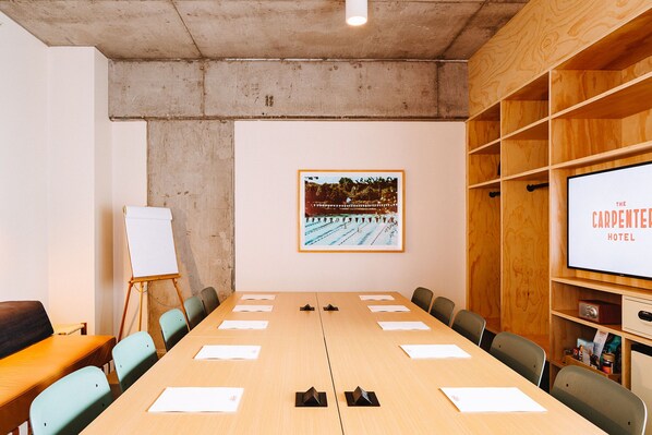 Une salle de conférence équipée d’une longue table, de chaises, d’un tableau blanc et d’un écran de projection sur lequel est affiché le nom « The Carpenter Hotel ».