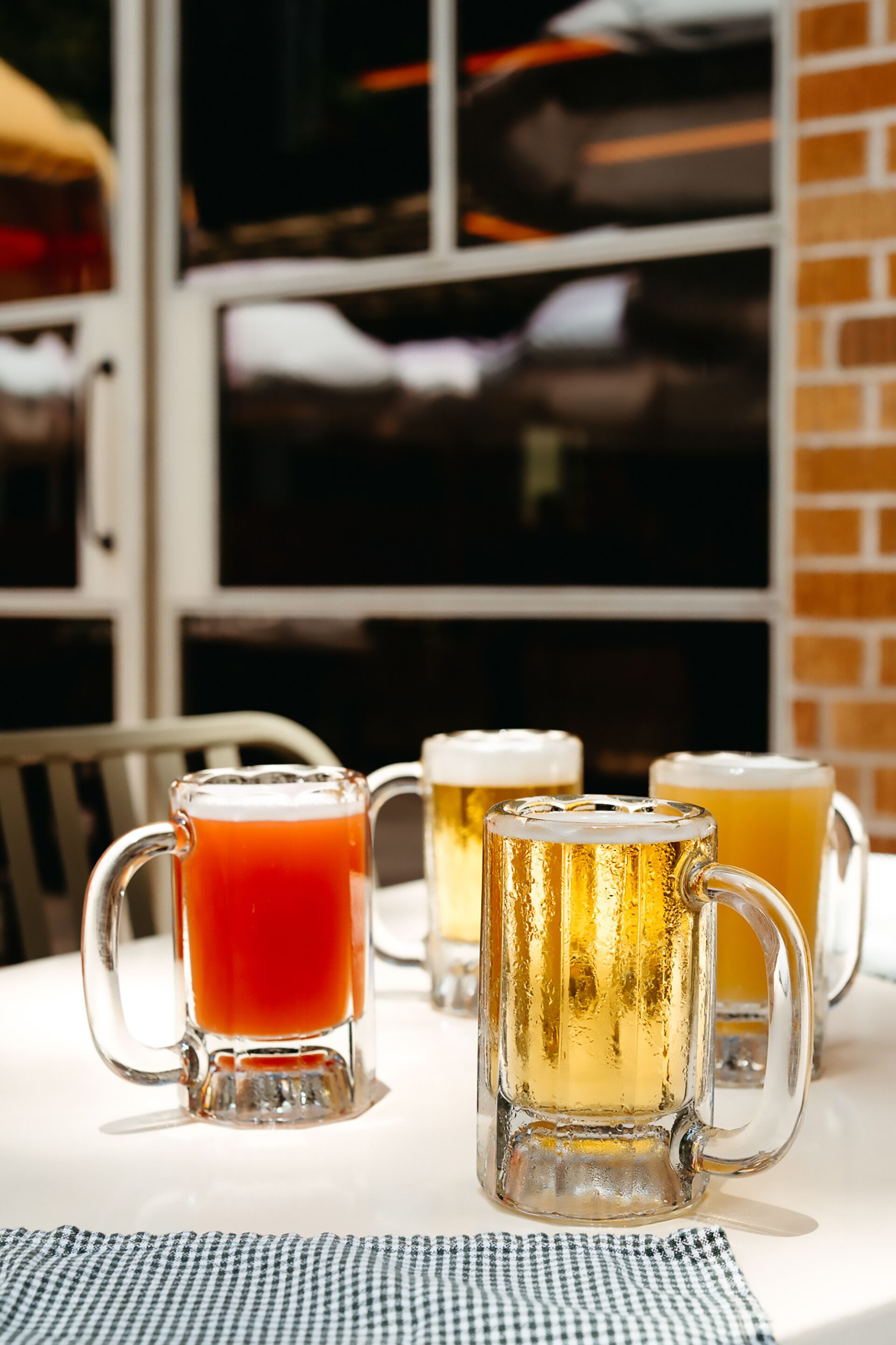 Three glass mugs on a table with a checkered tablecloth.