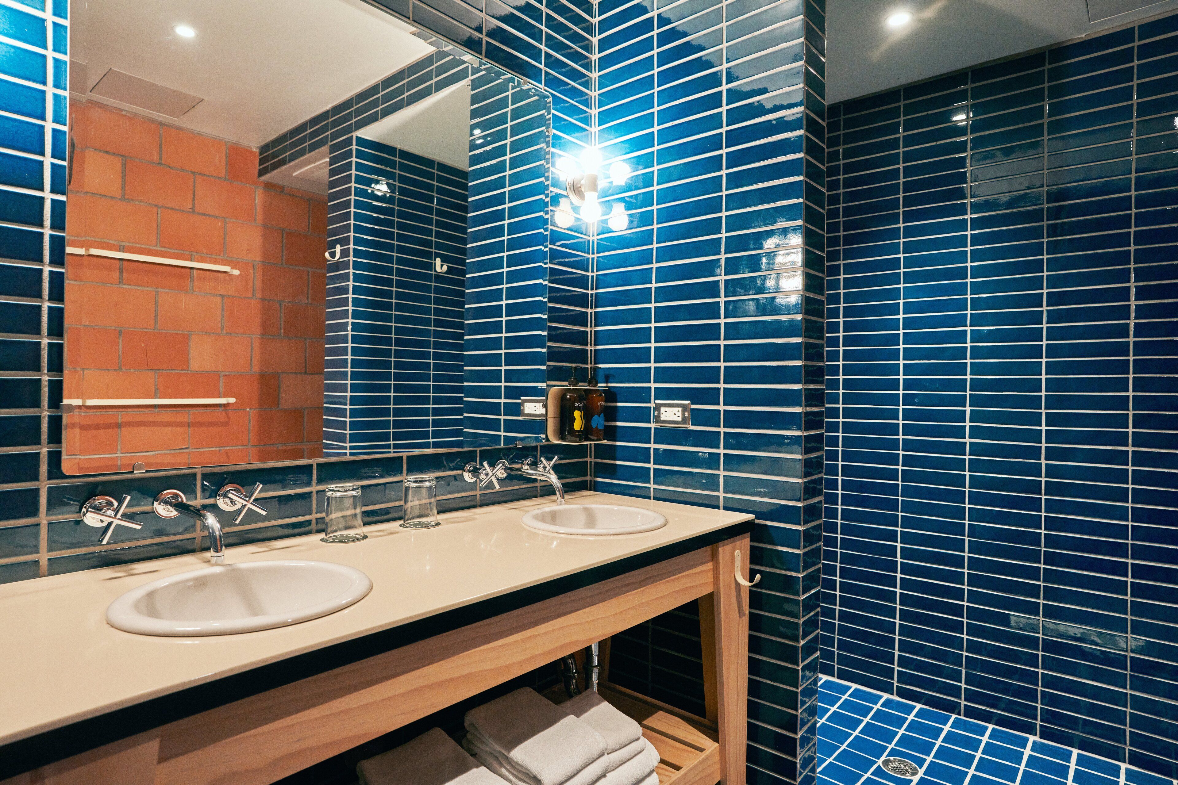 A bathroom with two sinks, a mirror, and blue-tiled walls.