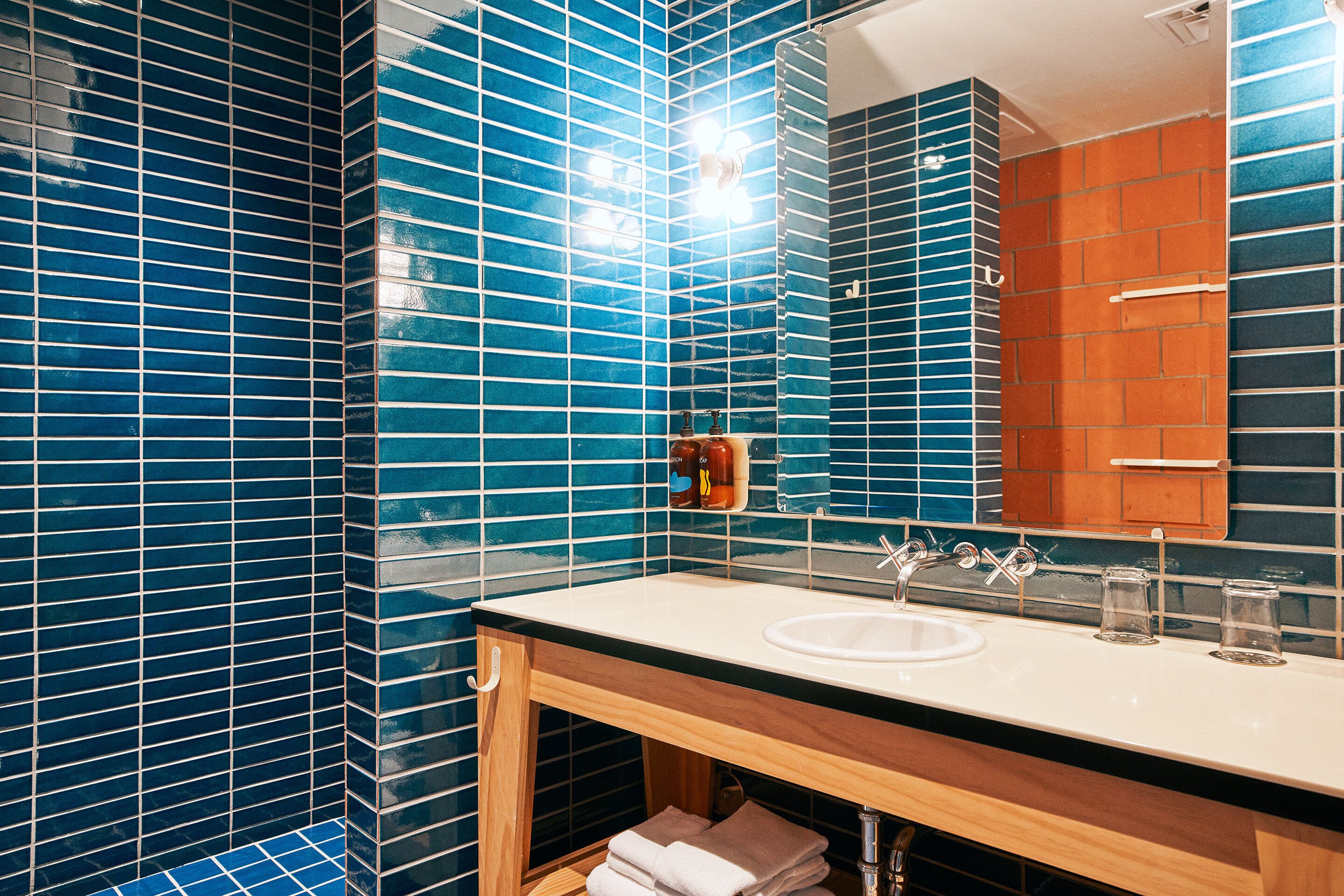 A bathroom with blue-tiled walls, a wooden vanity, a sink, and a mirror.