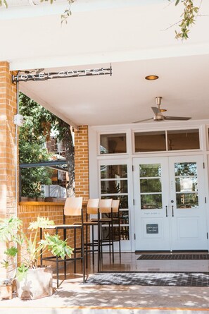 A hotel entrance with a glass door, a ceiling fan, and outdoor seating with chairs and a table.