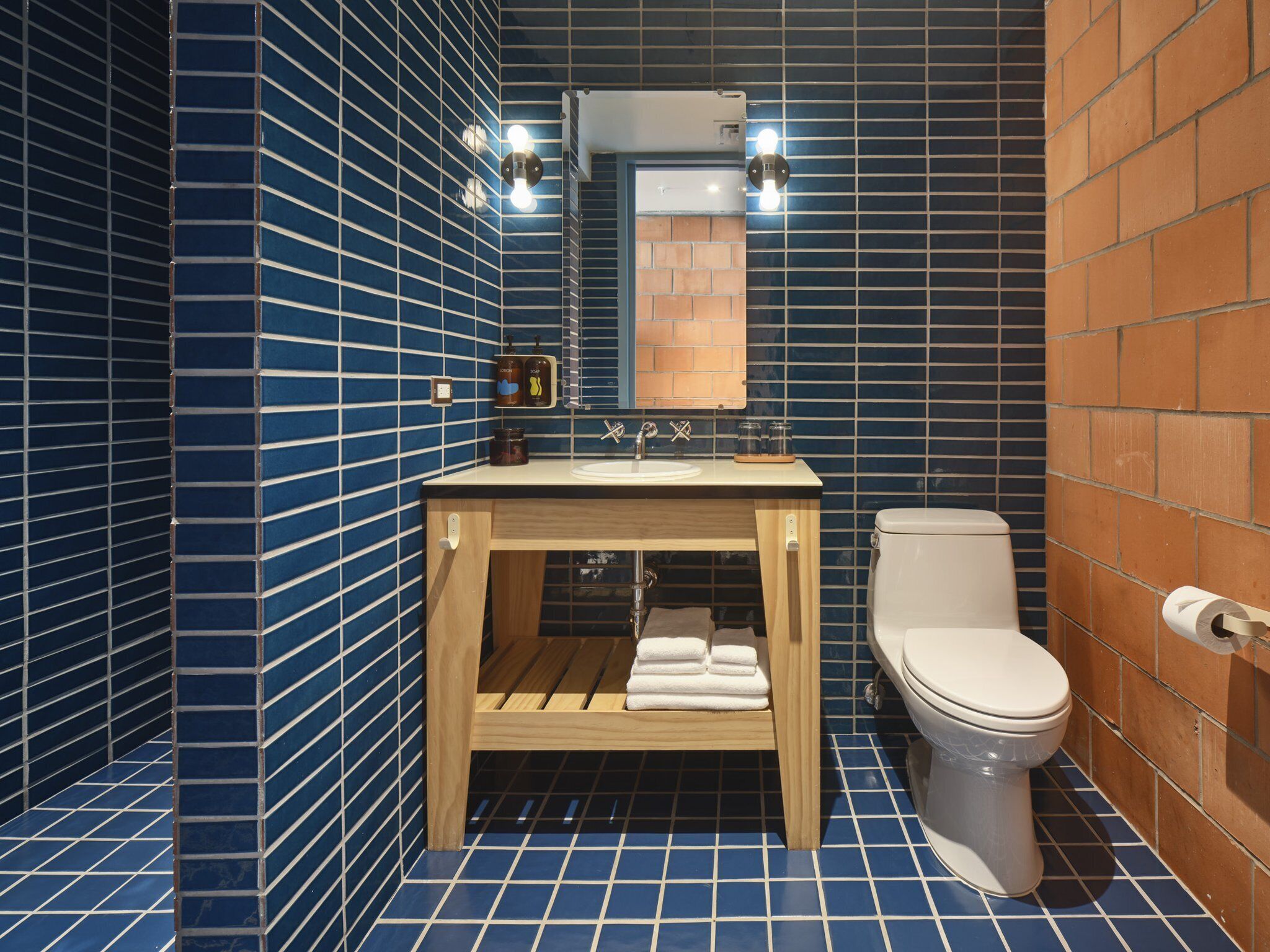 A bathroom with a blue tiled floor and walls, a wooden vanity with a sink and mirror, a toilet, and a towel rack.