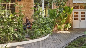 A hotel with a brick facade, large windows, and a garden area with various plants. - The Carpenter Hotel (Austin)