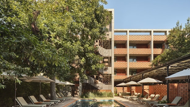 A swimming pool with lounge chairs and umbrellas, surrounded by trees and a multi-story building with a patterned facade. - The Carpenter Hotel (Austin)