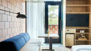 Habitació d'hotel amb paret de maó, un sofà, una taula petita amb una làmpada, una televisió i un mini-frigorífic.