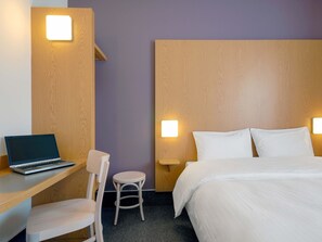 A hotel room with a bed, a desk with a laptop, a chair, and two wall-mounted lights. - B&B Hotel Prague-City (Prague)