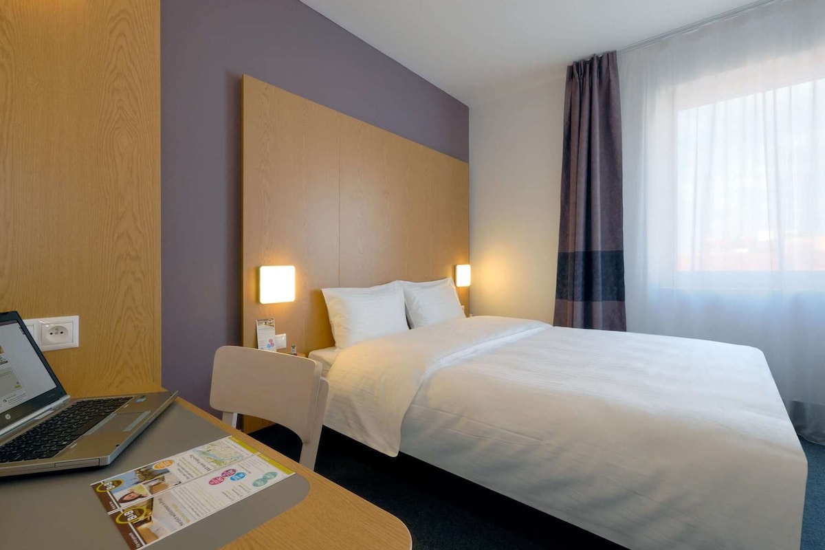 Une chambre d’hôtel avec un lit, une table de chevet, une lampe et un ordinateur portable sur le bureau.