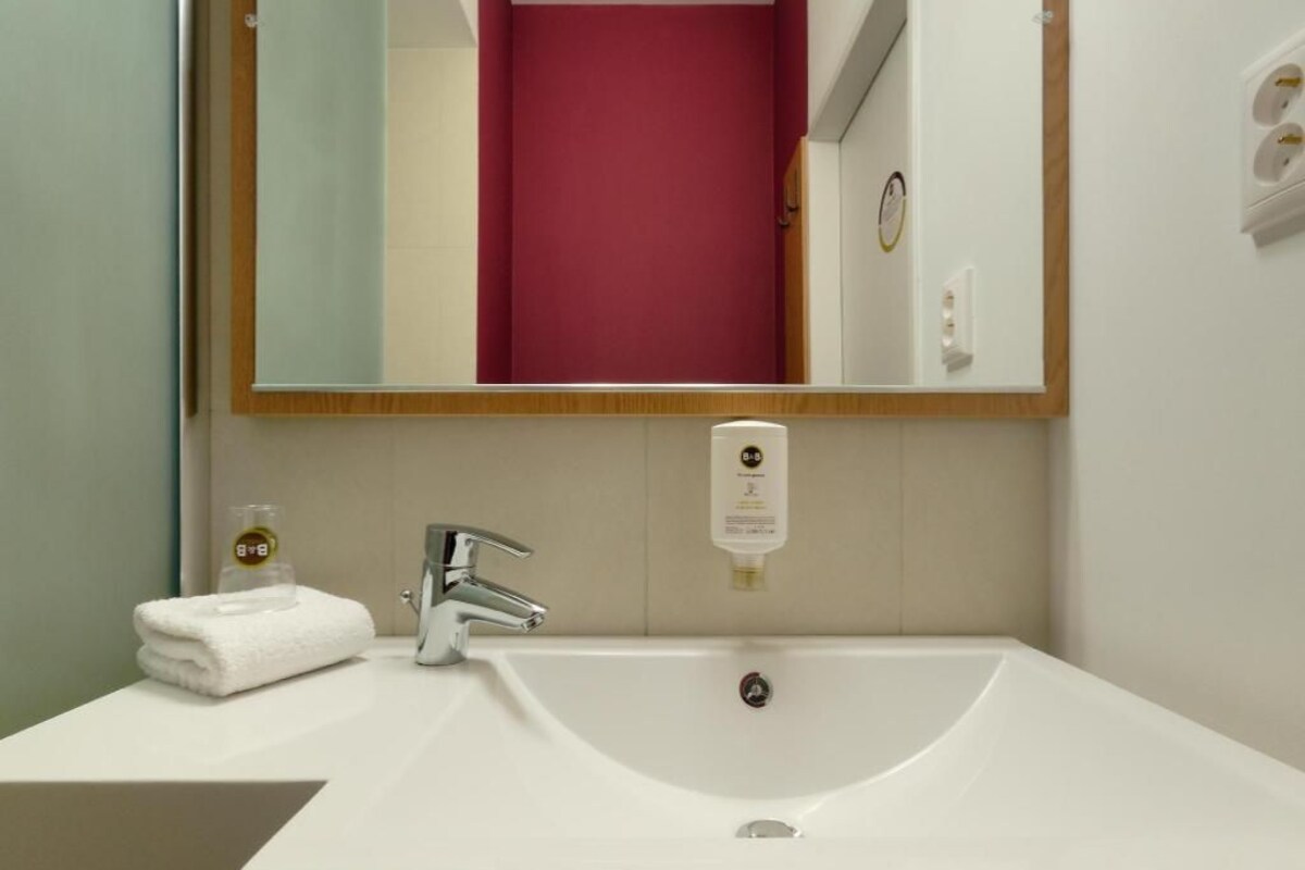 Une salle de bain avec un lavabo blanc, un miroir, une serviette et un distributeur de savon.
