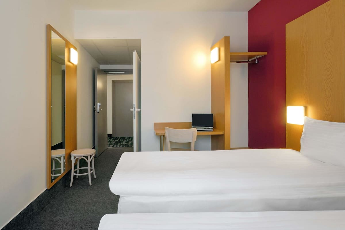 Ein Hotelzimmer mit einem Bett, einem Schreibtisch mit einem Laptop, einem Stuhl und einem kleinen Hocker.