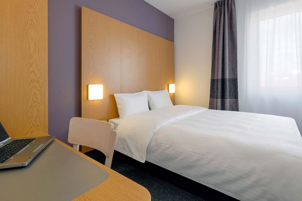 Ein Hotelzimmer mit einem Bett, einem Schreibtisch mit einem Laptop und einem Sessel.