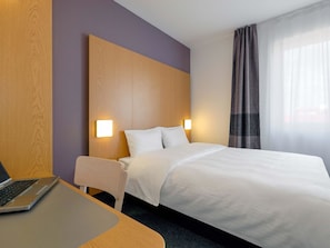 Ein Hotelzimmer mit einem Bett, einem Schreibtisch mit einem Laptop und einem Sessel.