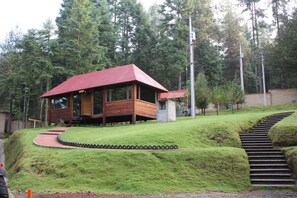 A wooden cabin with a red roof, surrounded by a grassy area and a stone staircase leading up to it.