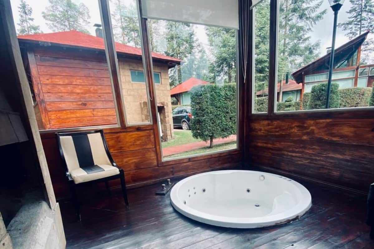 A wooden cabin with a hot tub, large windows, and a chair.