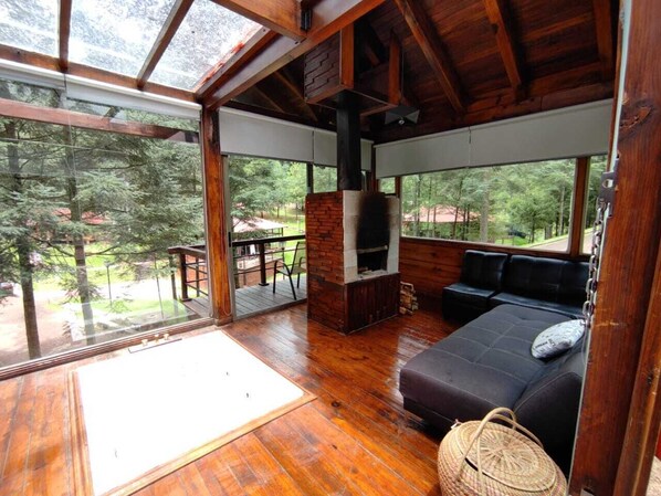 A cozy cabin with a wooden interior, a fireplace, a sofa, and a large window overlooking a forested area.