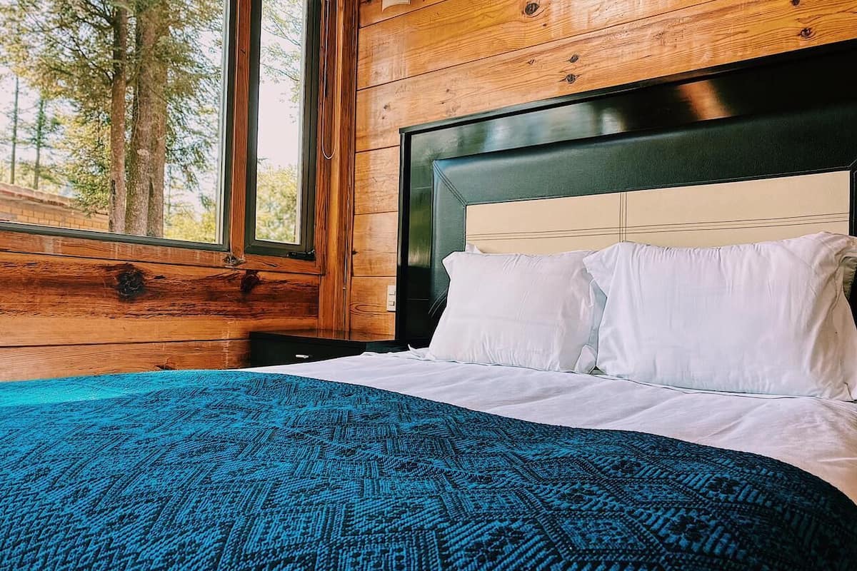 A bedroom with a large bed, wooden walls, and a window overlooking trees.