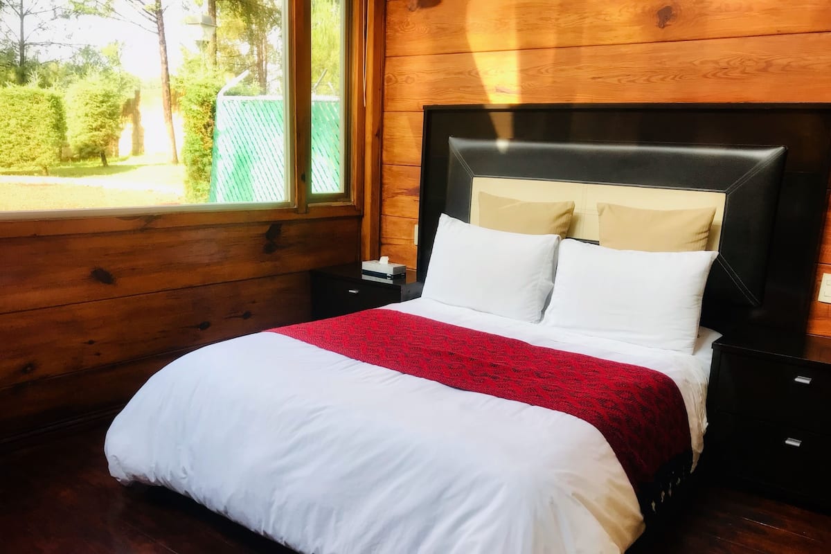 A neatly made bed with white and red bedding, a wooden headboard, and a nightstand with a lamp.