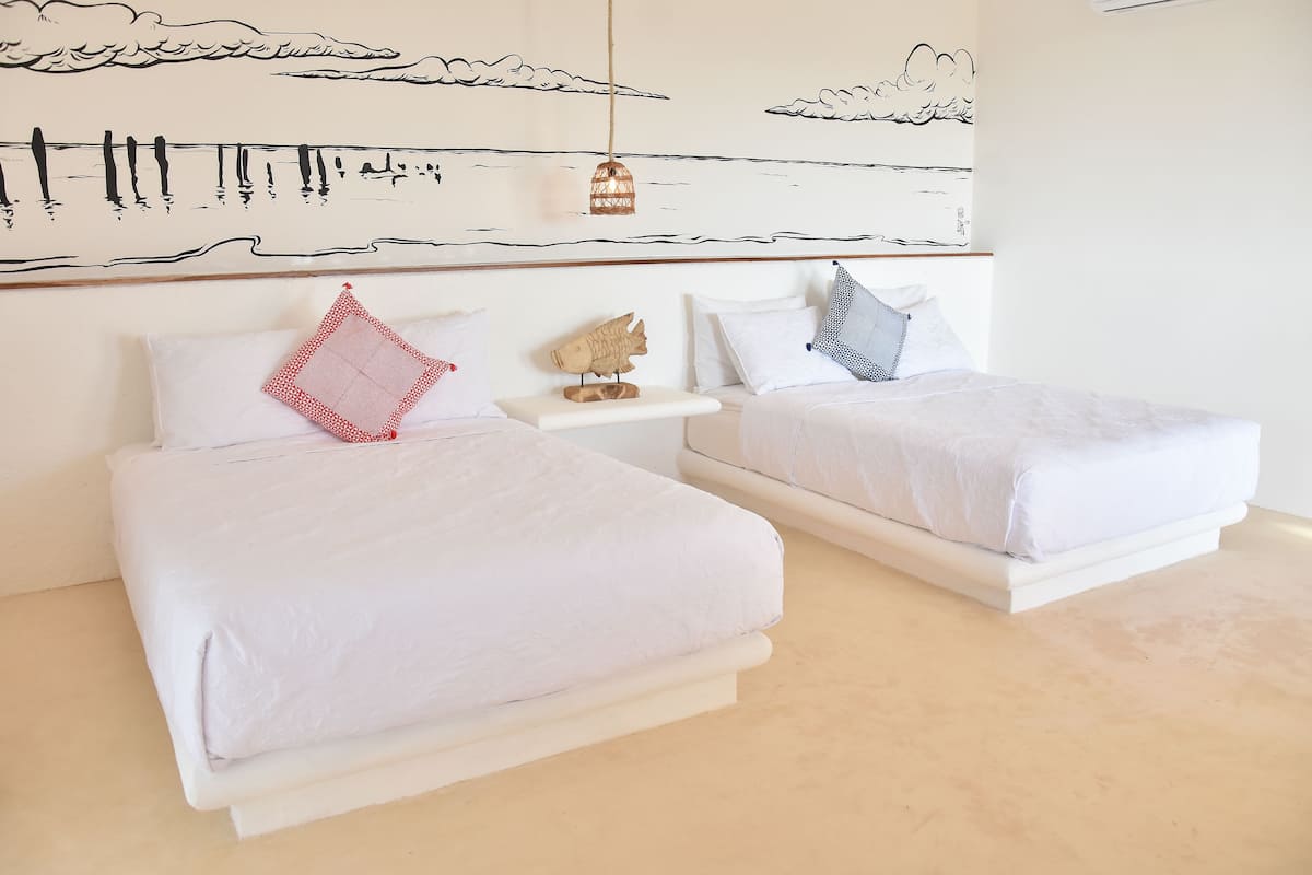 Una habitación de hotel con dos camas, una mesita de noche pequeña y un mural en la pared.